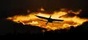 A small plane seen as a dark shape against an orange sunset sky