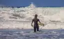 A surfer in a wetsuit wading into white waves with a board