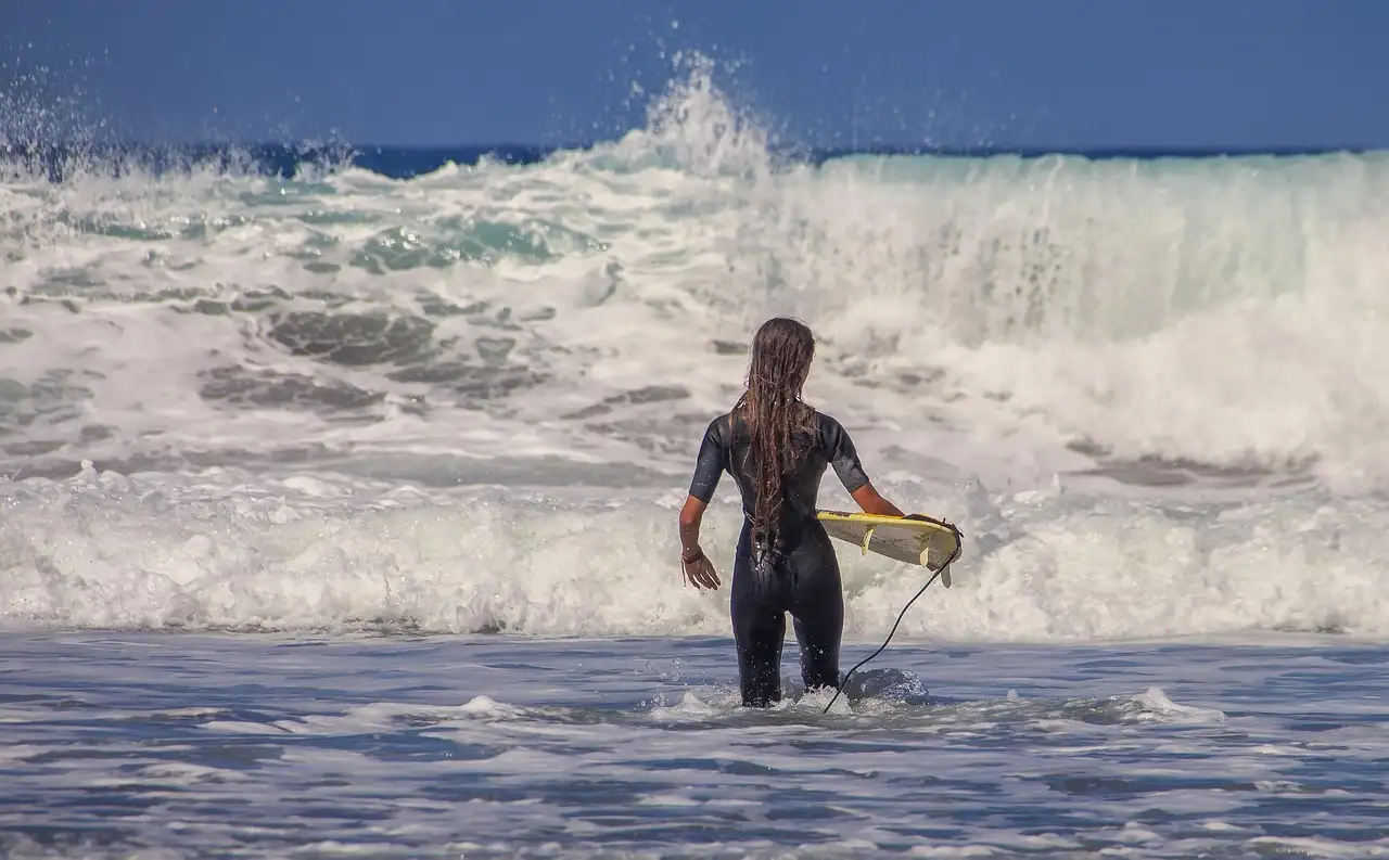 A surfer in a wetsuit wading into white waves with a board