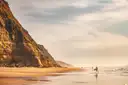 Surfers walking on a beach below tall sandstone cliffs