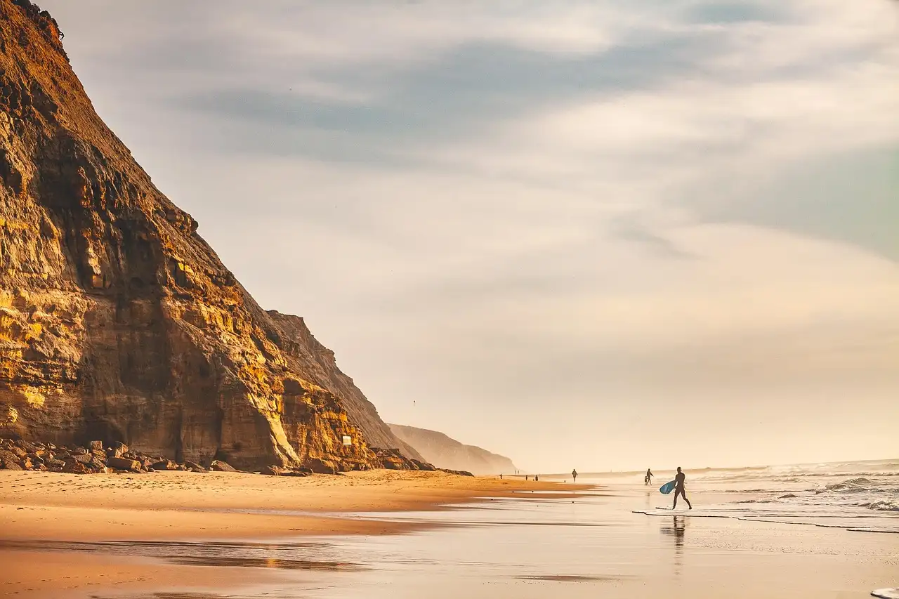 Surfers walking on a beach below tall sandstone cliffs