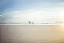 Two surfers carrying boards across a wide, flat beach