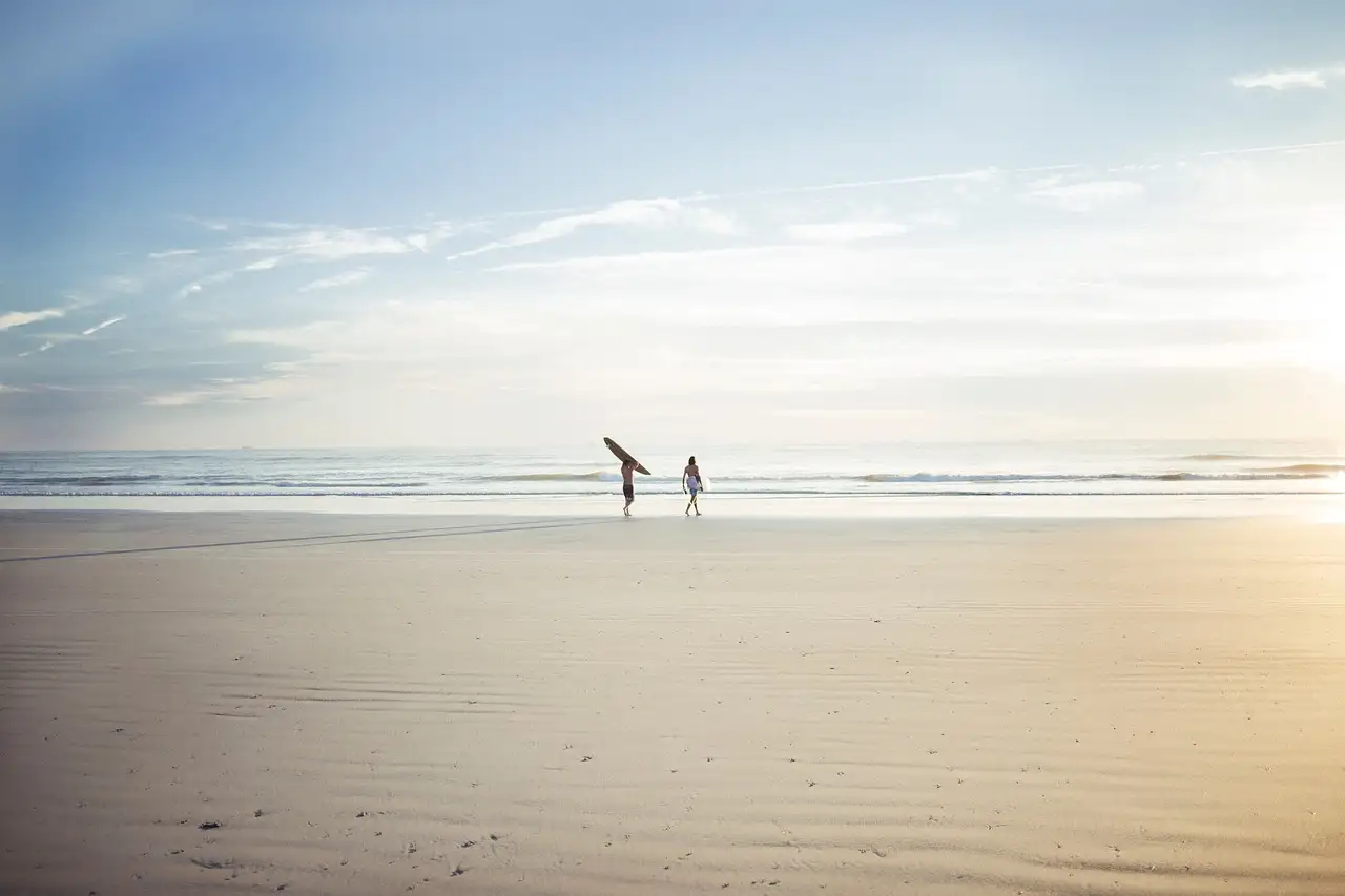 Two surfers carrying boards across a wide, flat beach