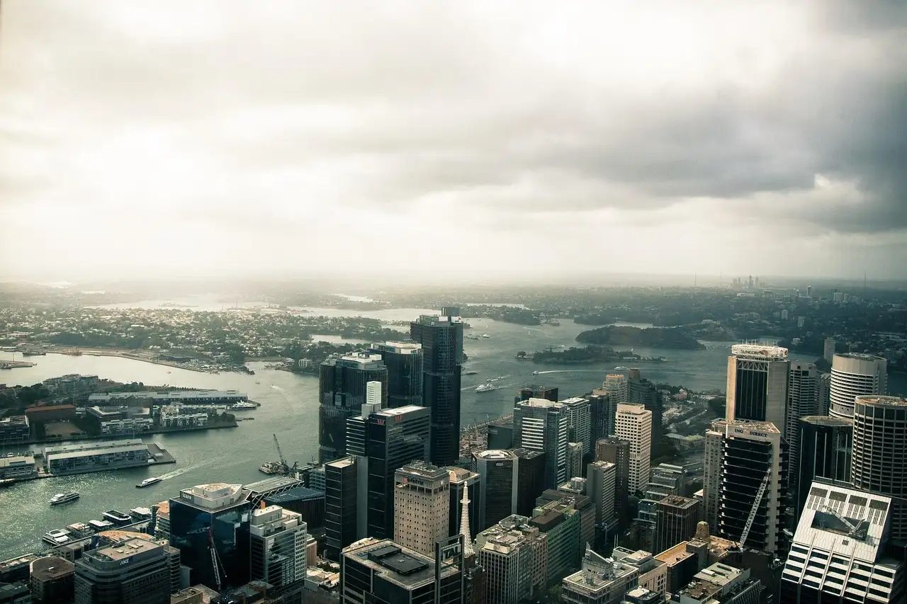 Sydney's city towers seen from above, with the harbour behind under a cloudy sky