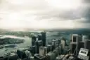 Sydney's city towers seen from above, with the harbour behind under a cloudy sky