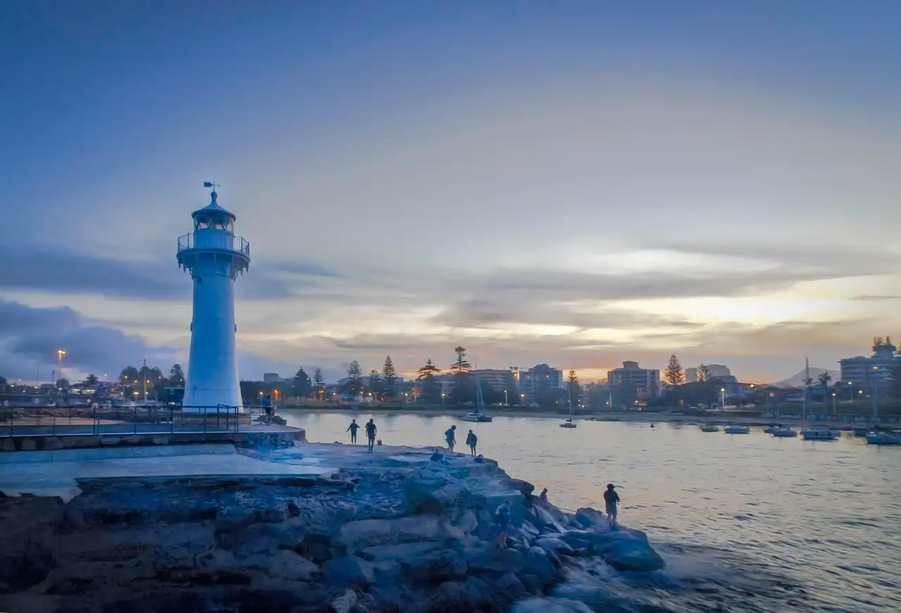 A white lighthouse on a rocky breakwater beside the harbour at Wollongong at dusk
