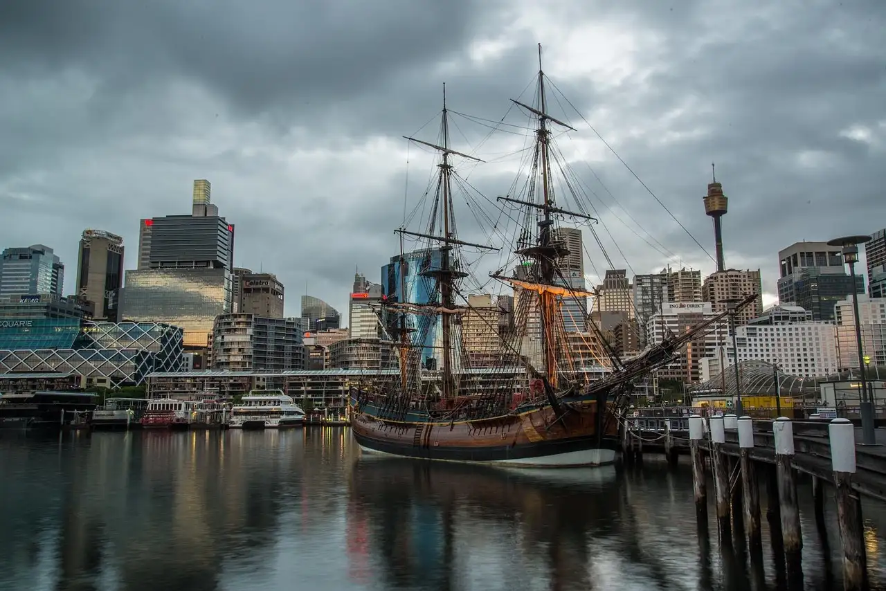 A wooden tall ship moored at a wharf in Sydney under a cloudy sky