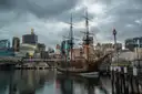 A wooden tall ship moored at a wharf in Sydney under a cloudy sky