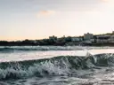 A wave breaking on a Sydney beach at dusk with the coastline behind