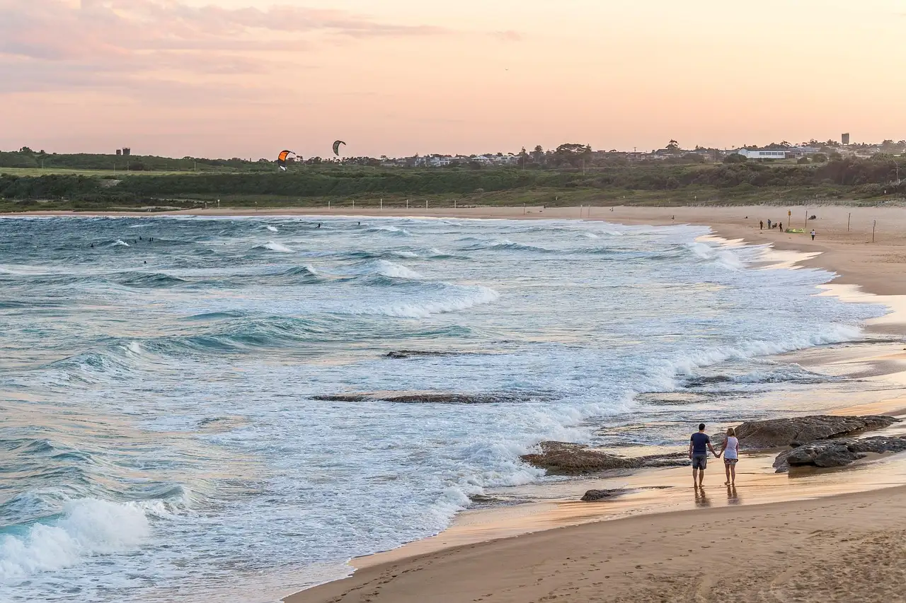 Two people walking along a Sydney beach at sunset beside rolling waves