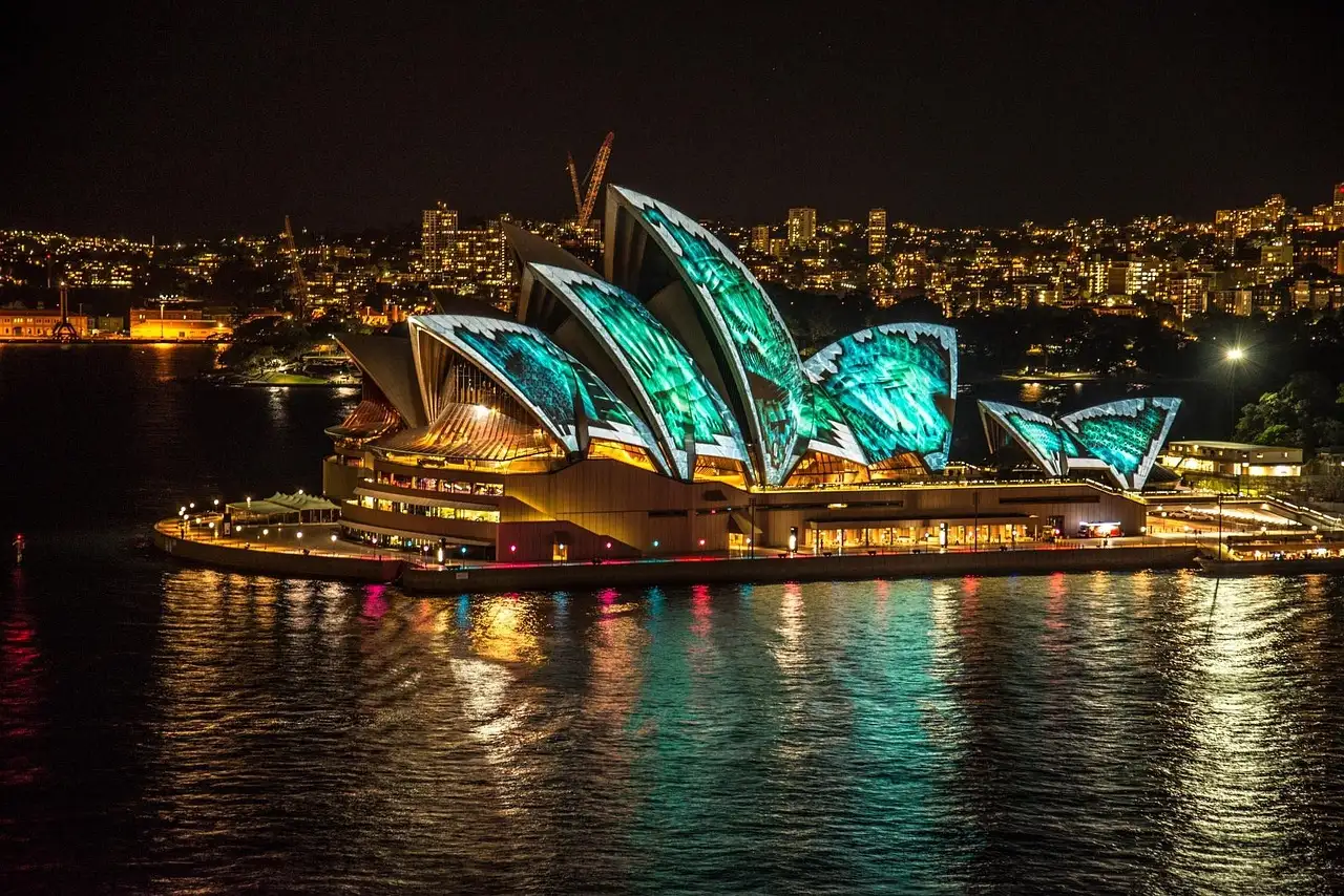 The Sydney Opera House lit with colourful light projections at night, reflected in the harbour