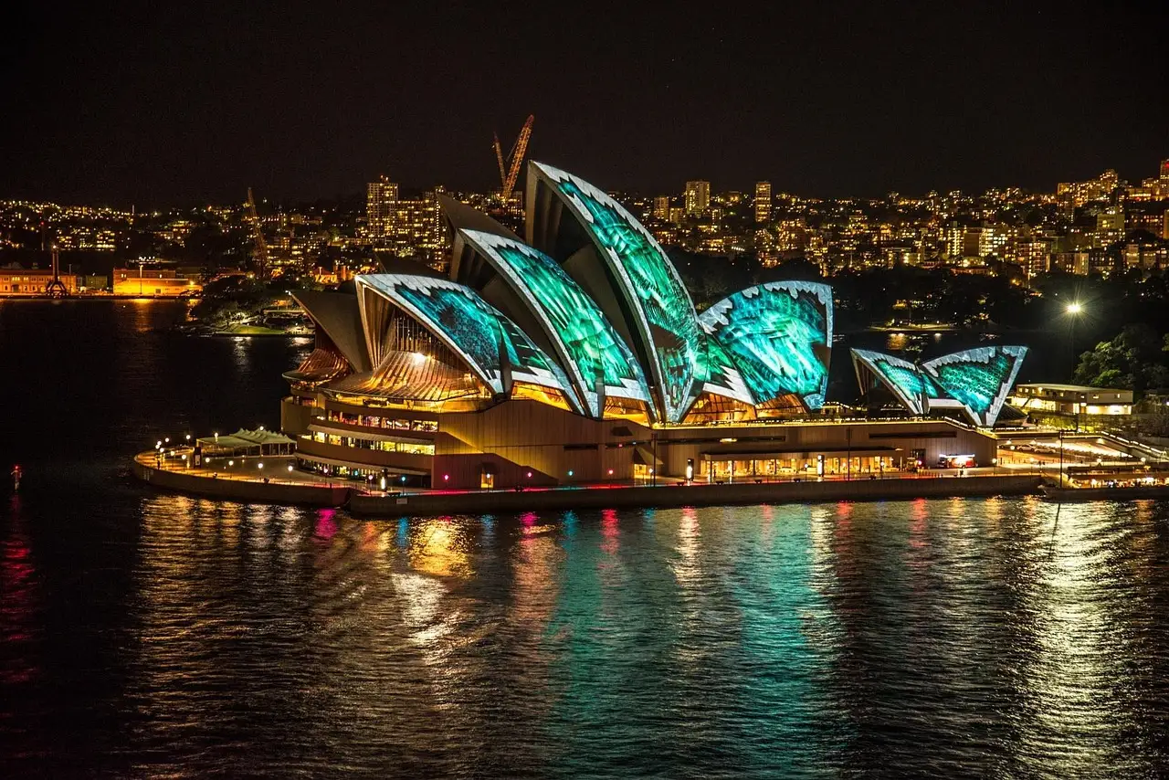 The Sydney Opera House lit with colourful light projections at night, reflected in the harbour