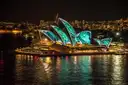 The Sydney Opera House lit with colourful light projections at night, reflected in the harbour
