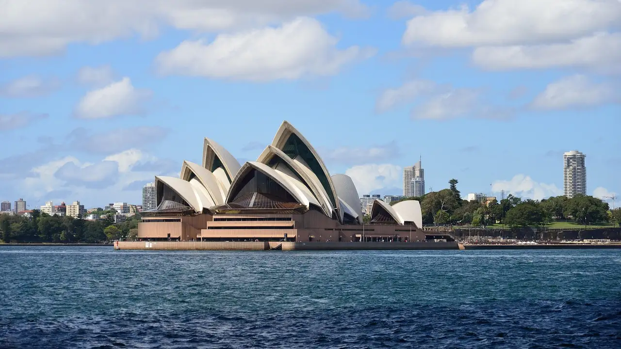 The Sydney Opera House across blue harbour water on a sunny summer day