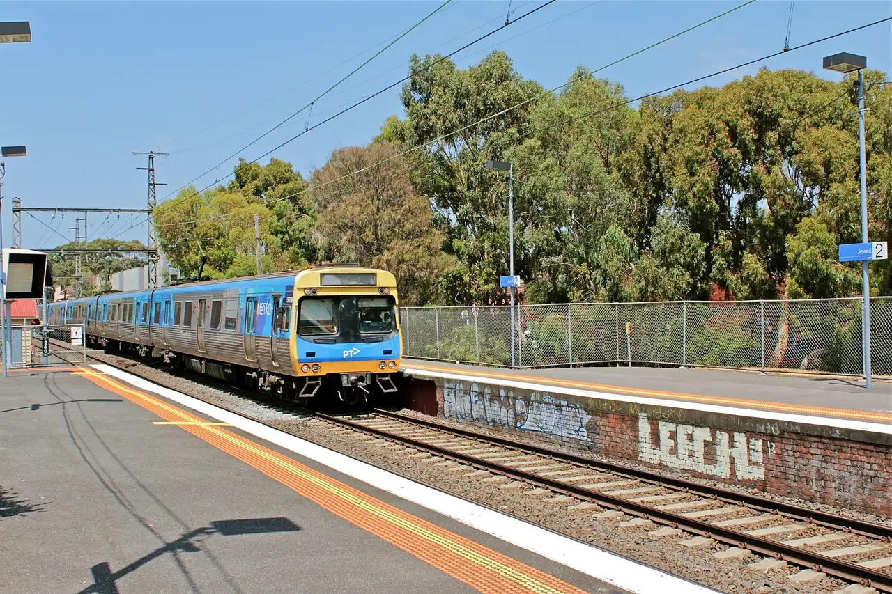 A suburban passenger train at a platform beside gum trees under a blue sky