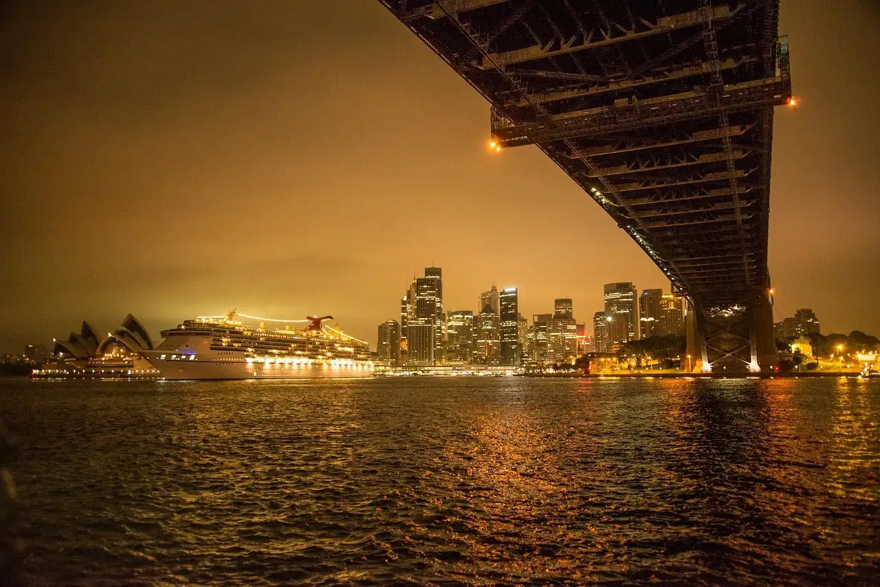 The underside of the Sydney Harbour Bridge at night, with the lit city across the water